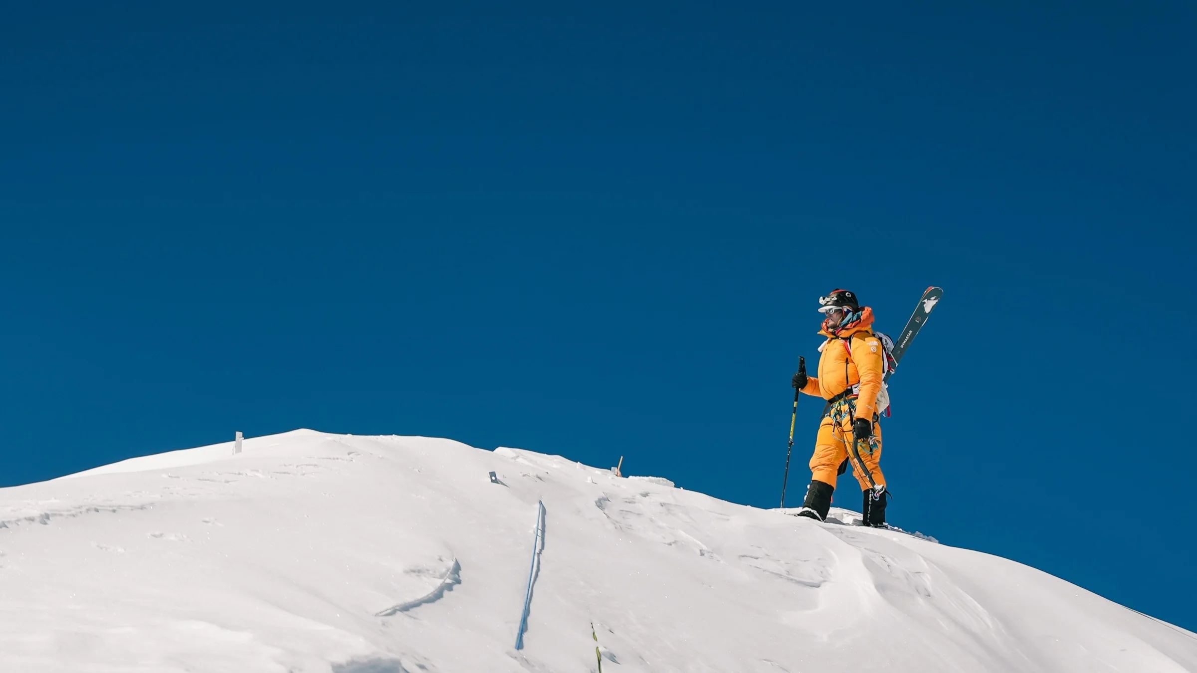A ski mountaineer carrying skis on a summit ridge against a deep blue sky