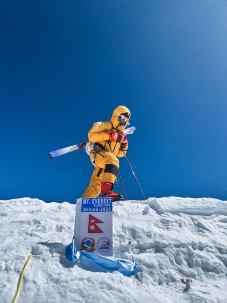 Narciarz z nartami na plecach przy tabliczce szczytowej Mount Everestu
